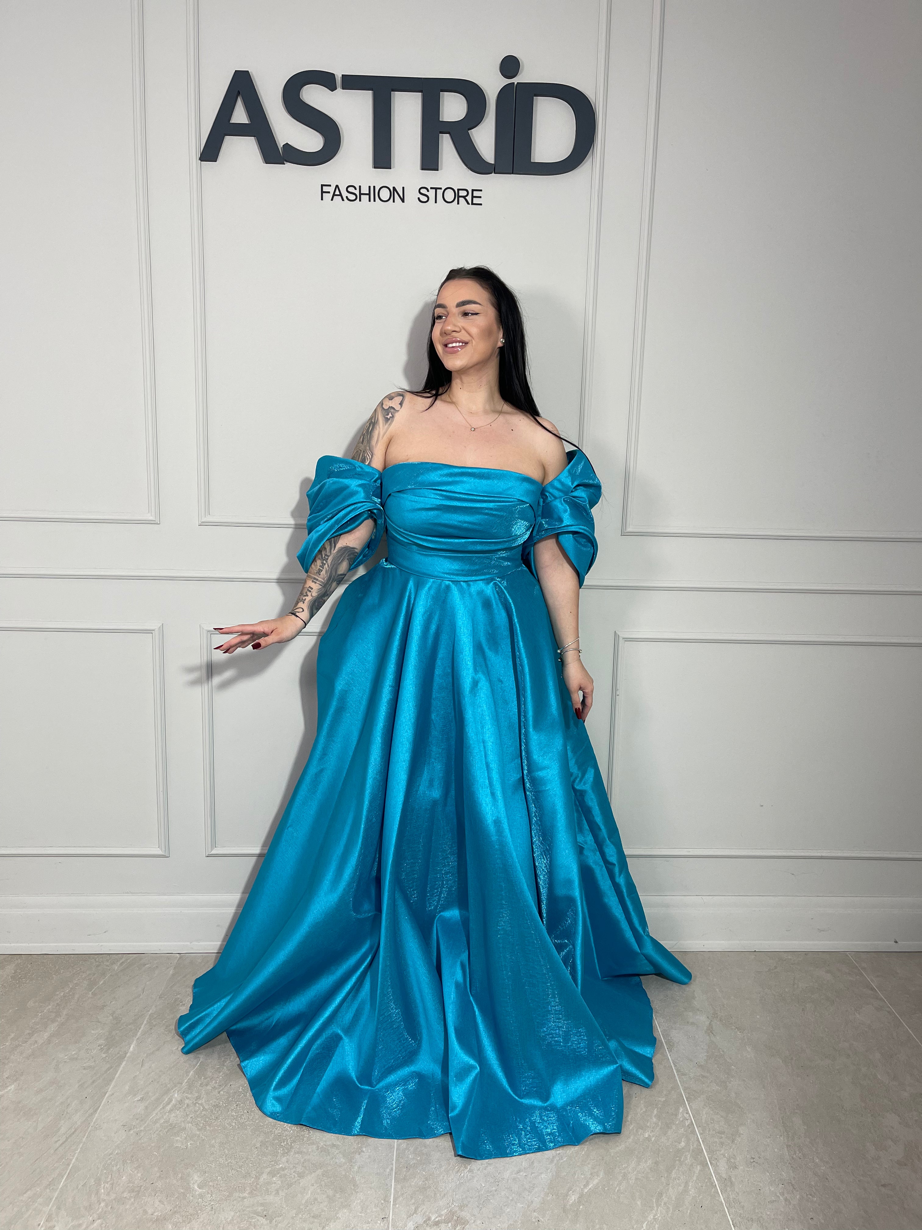 Rochie Lora lungă, intr-un albastru deschis delicat, cu umeri goi ce subliniază eleganța și feminitatea.