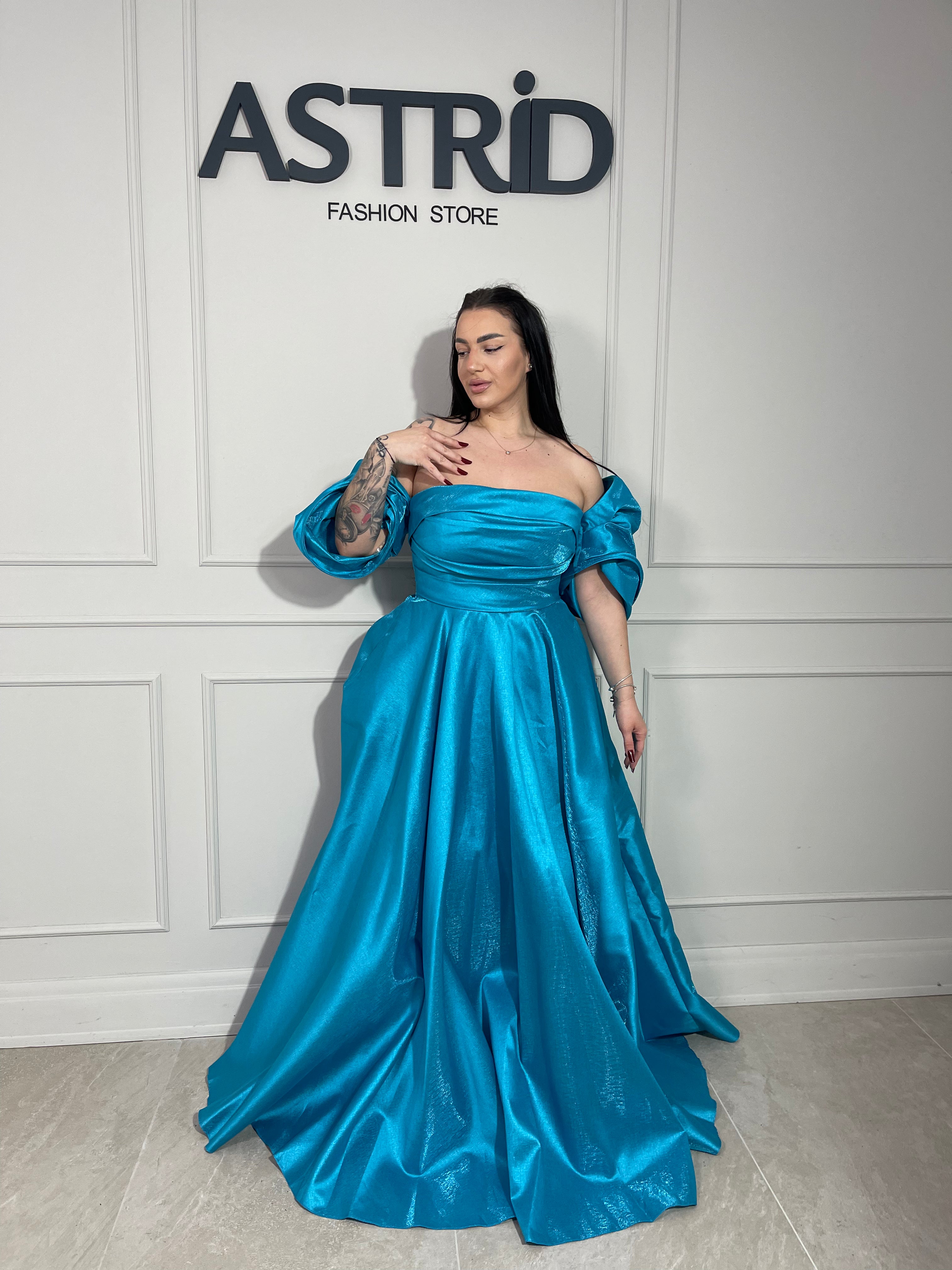 Rochie Lora lungă, intr-un albastru deschis delicat, cu umeri goi ce subliniază eleganța și feminitatea.