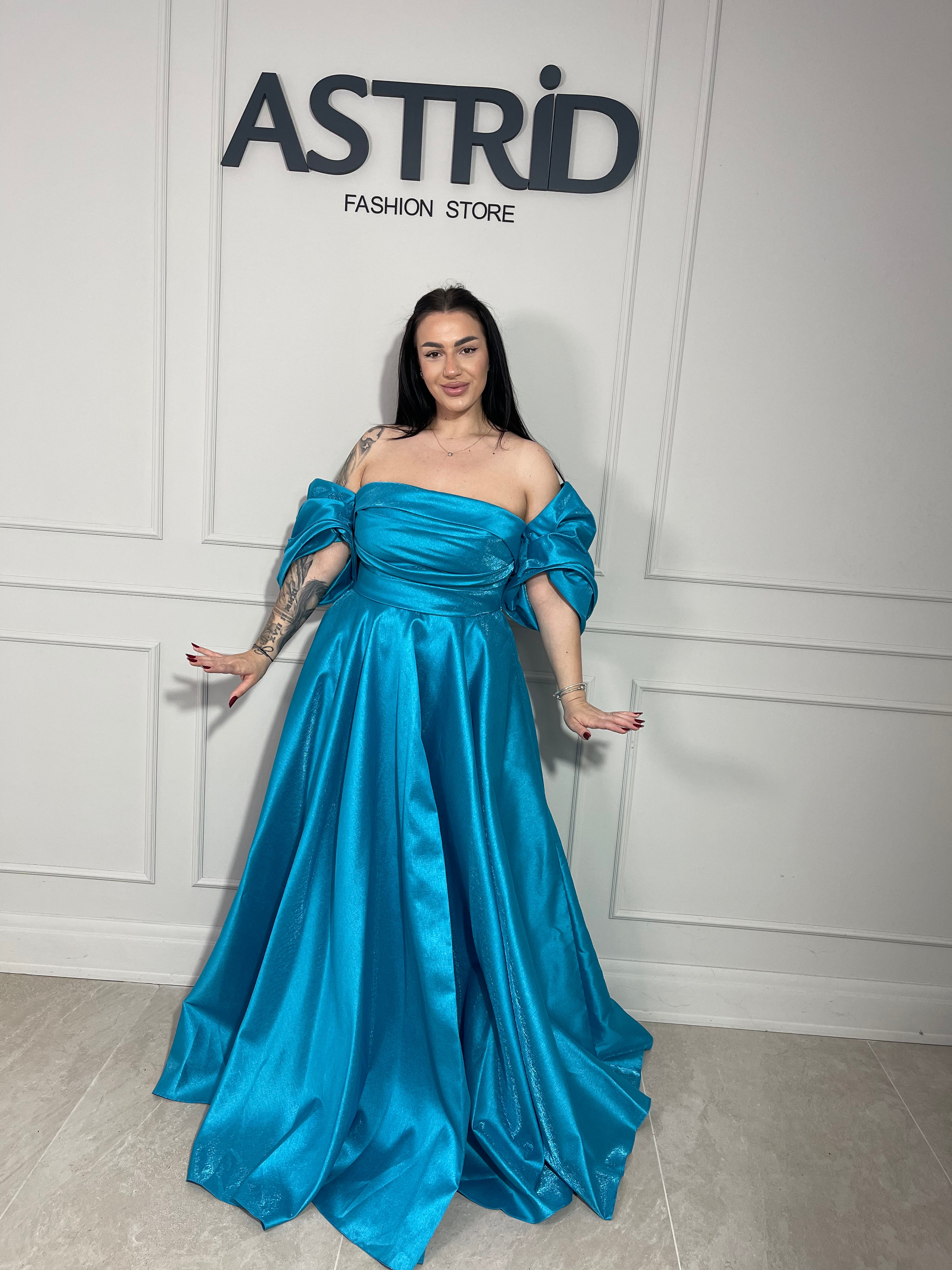 Rochie Lora lungă, intr-un albastru deschis delicat, cu umeri goi ce subliniază eleganța și feminitatea.