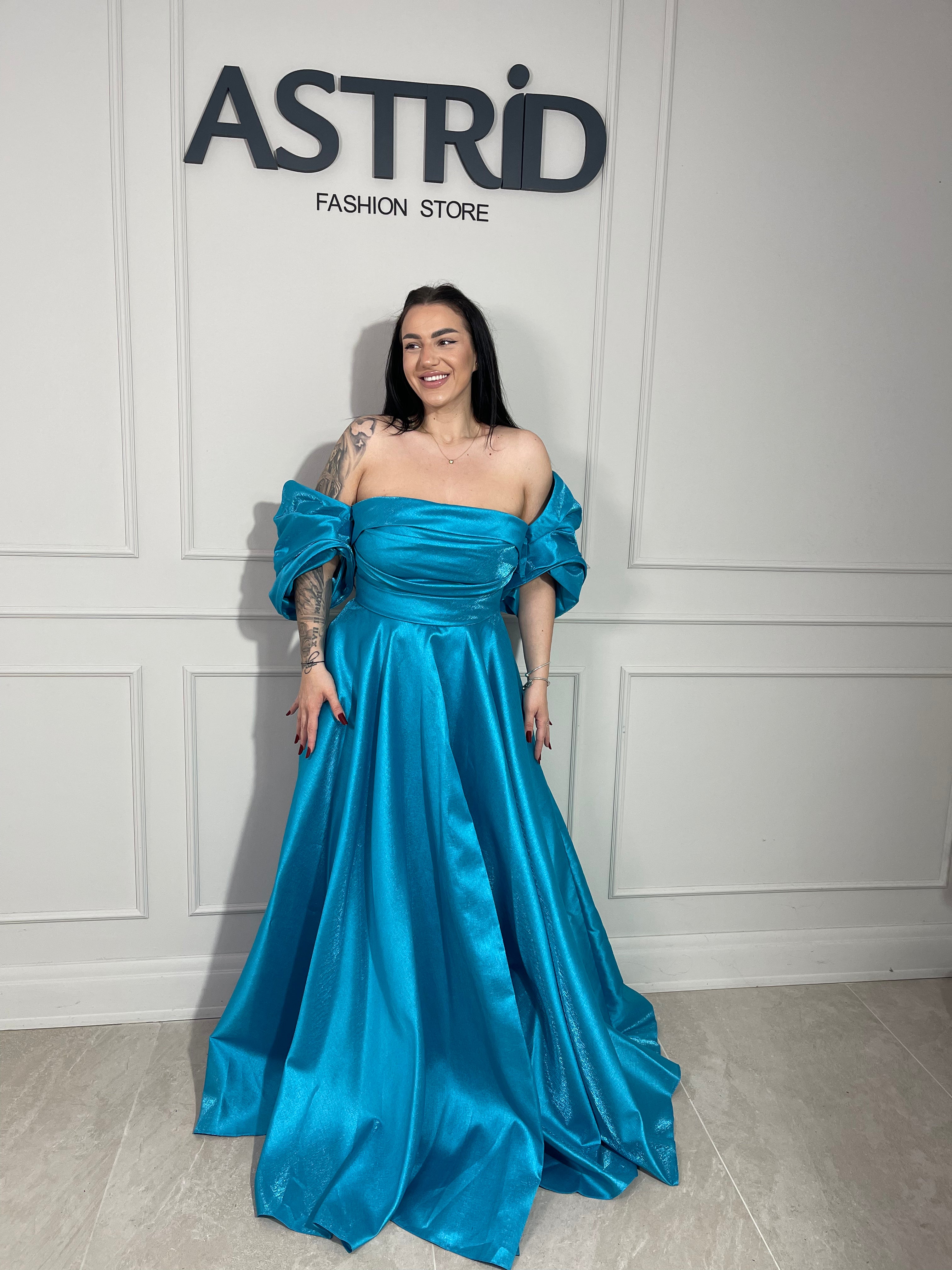 Rochie Lora lungă, intr-un albastru deschis delicat, cu umeri goi ce subliniază eleganța și feminitatea.